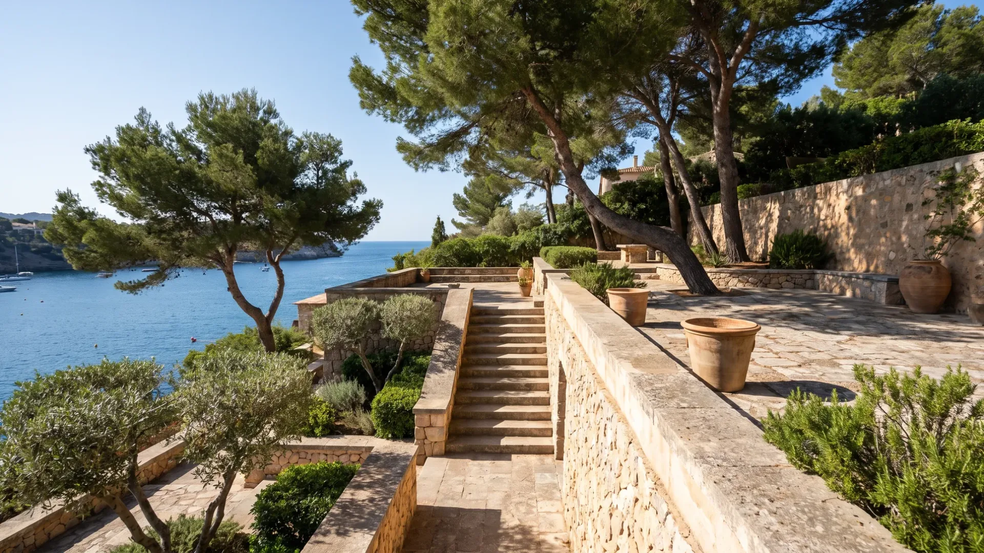 Terraced garden platforms held by stone retaining walls dropping towards the bay at Costa d'en Blanes