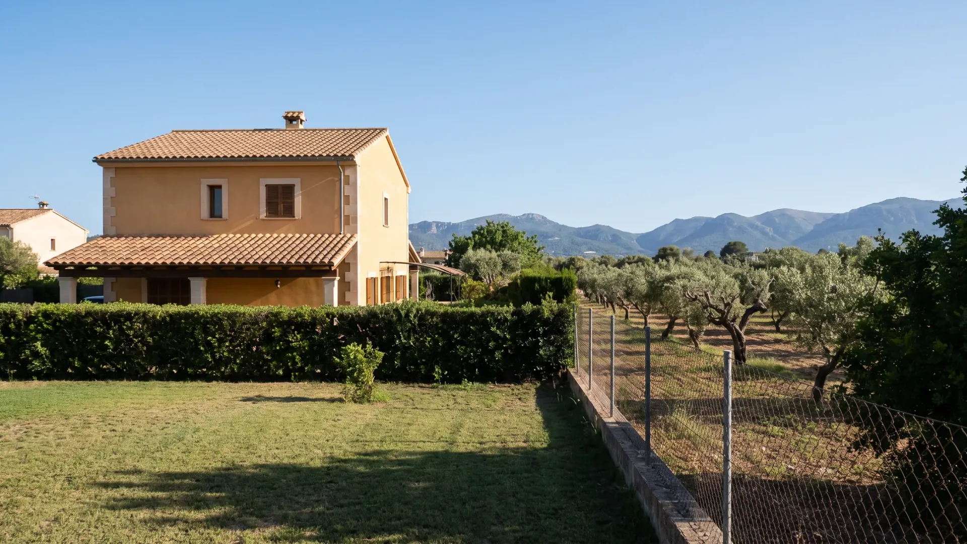 A newer house at the edge of Inca with lawn and boundary hedge, almond farmland and the foothills beyond