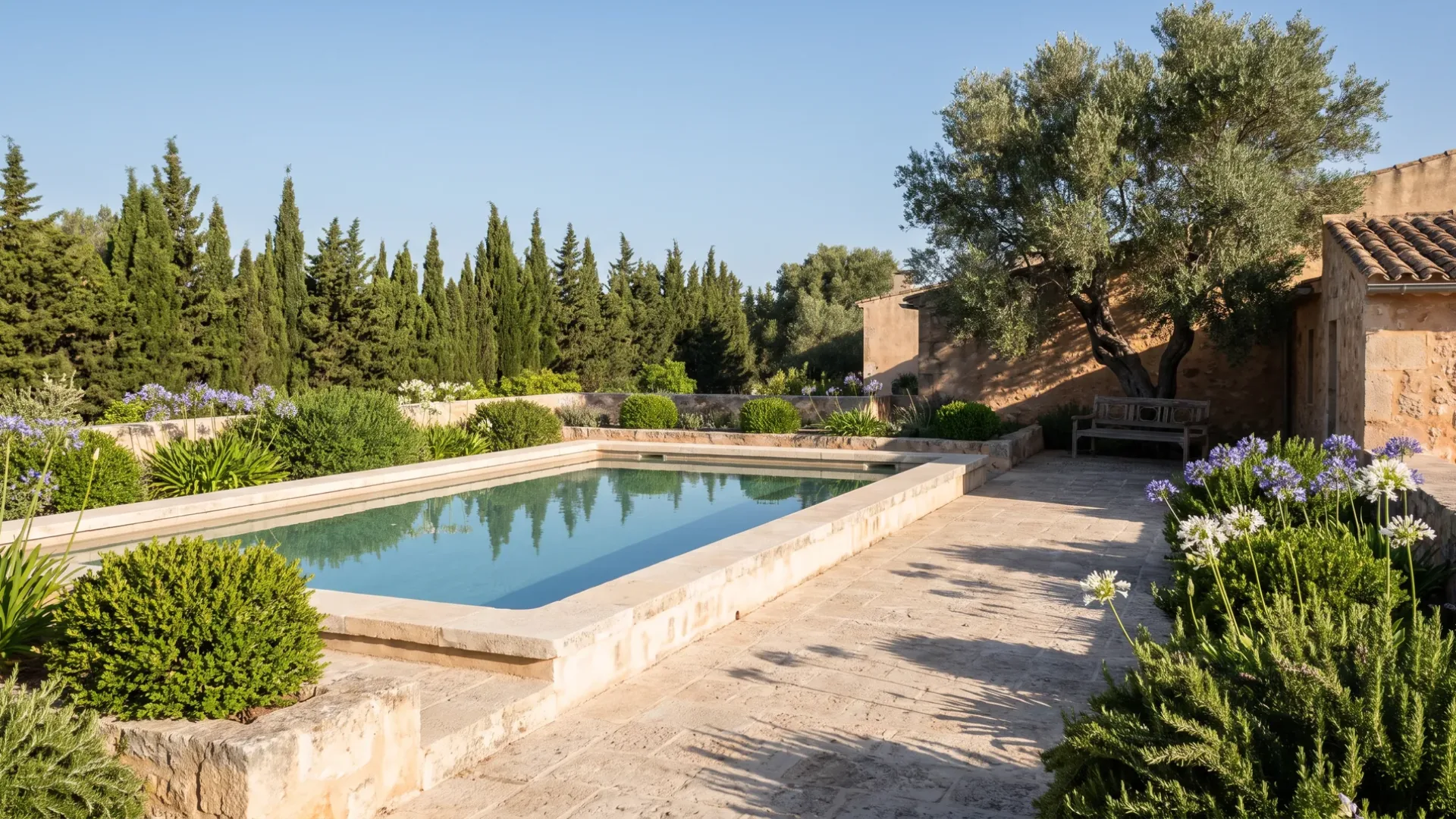 A rectangular pool with limestone coping, low litter planting and a cypress screen at a Mallorcan villa