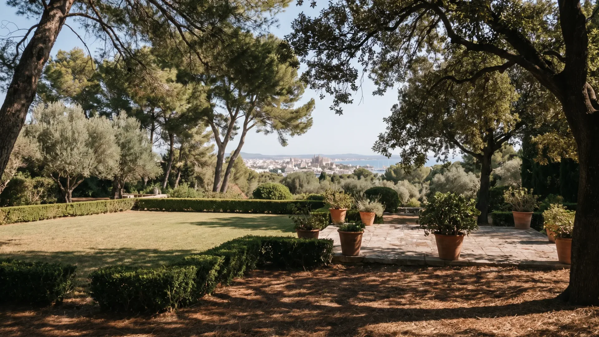 A large lawn under mature pine and holm oak at Son Vida, with Palma and the bay in the distance
